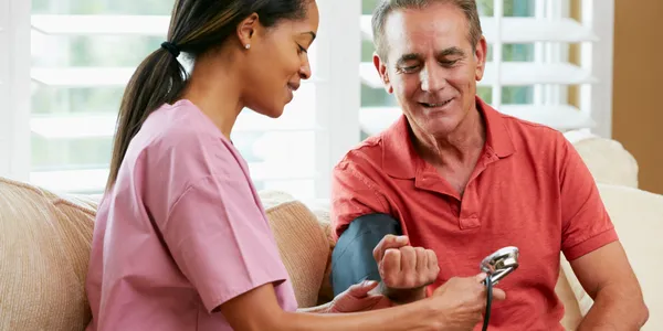 Professional home health nurse checking blood pressure of a senior man during a home visit