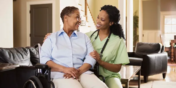 Compassionate home health aide supporting a smiling senior woman in a wheelchair