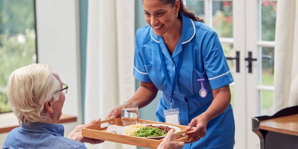 Female care worker bringing meal as part of home care service